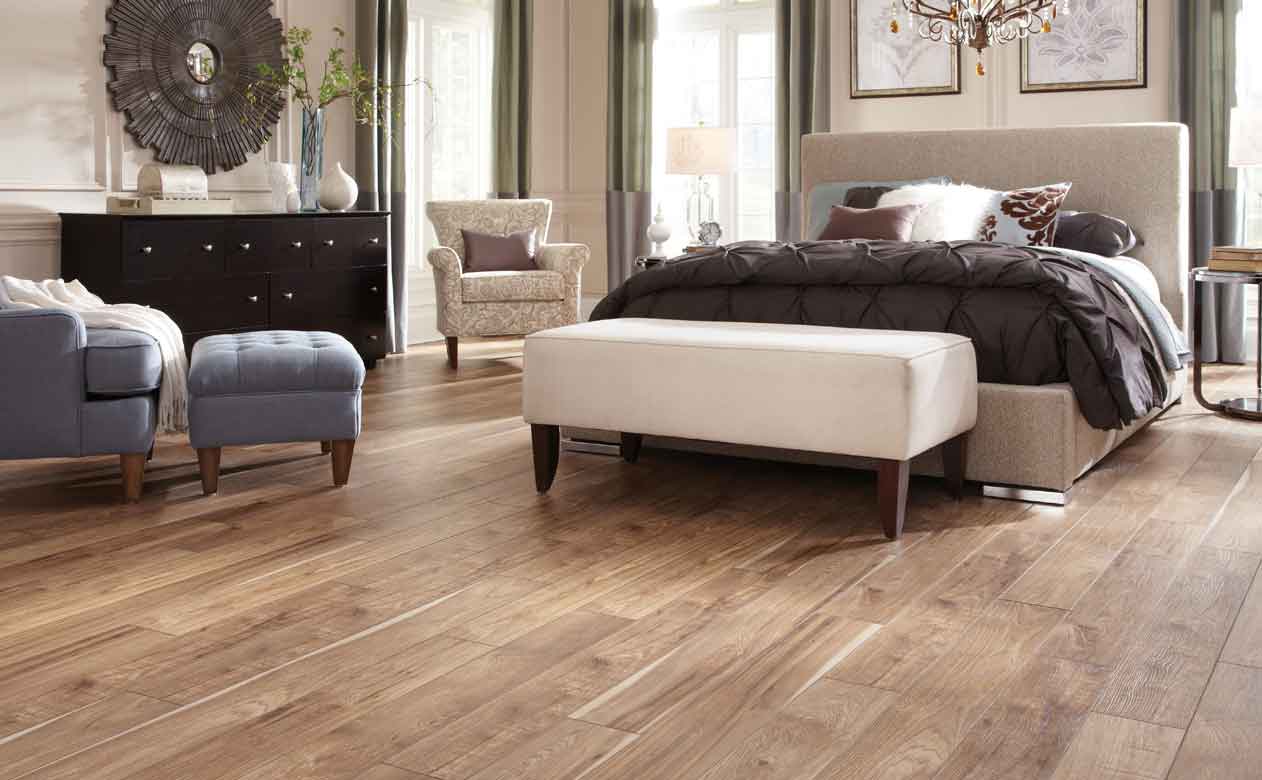 Bedroom with a large upholstered bed, wood-look tile flooring in natural brown tones, and elegant decor for a stylish, inviting space.