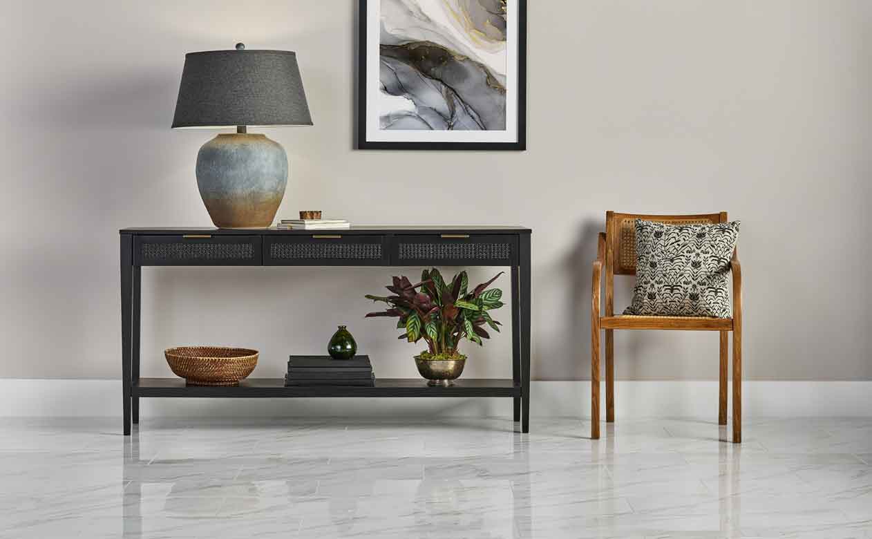 Entryways with a console table, abstract artwork, and a wooden chair, set against a light-colored wall with highly reflective, light-colored marble-look tiles featuring subtle veining